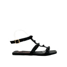 Black: EXE 2269-2781 pyramid stud T-strap flat sandal in black with gold-tone ankle buckle and square toe, side view