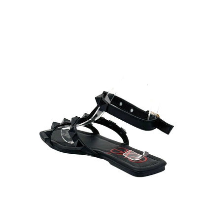 Black: EXE 2269-2781 pyramid stud T-strap flat sandal in black with gold-tone ankle buckle and square toe, side view